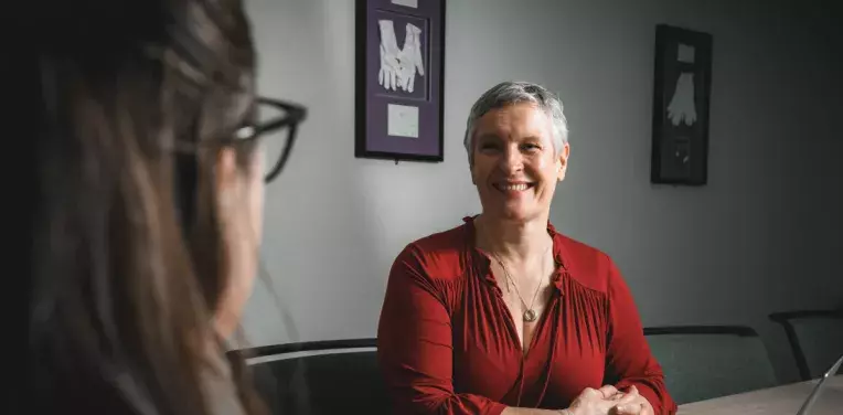Two people in conversation, on the table between them is a laptop and papers