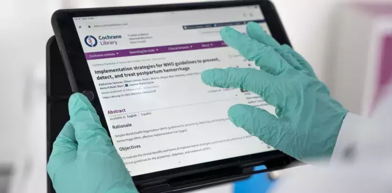 Hands holding tablet showing Cochrane Library site