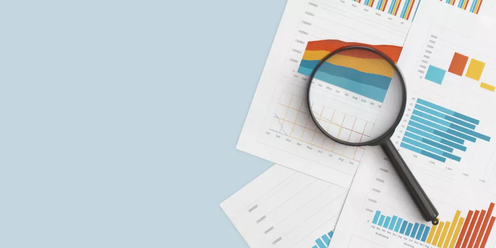 Business graphs, charts and magnifying glass on table.