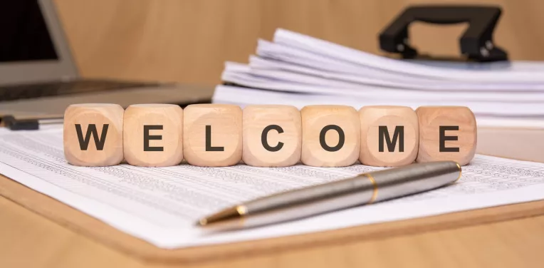 The word "welcome" is displayed with decorative wooden blocks in a professional office setting