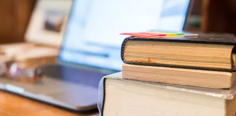 A laptop with the screen on, in front of it is a stack of books